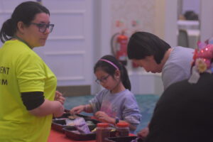 A child and an adult in a yellow T-shirt participating in an arts-and-crafts activity together."