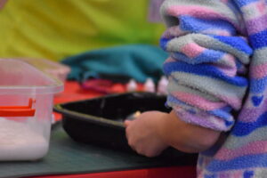 A close-up of someone preparing craft materials on a table covered with containers, coloured supplies, and tools."