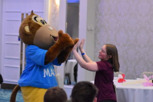 The MACS mascot giving a joyful high-five to a child in a bright room."
