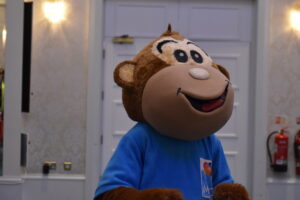 The MACS mascot standing happily in the room, engaging with the group."