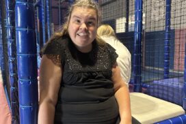 Person seated inside an indoor soft play area surrounded by padded climbing frames and netted play equipment."