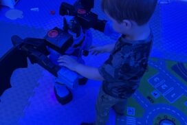 Child interacting with an illuminated sensory play station in a room lit with blue lighting."