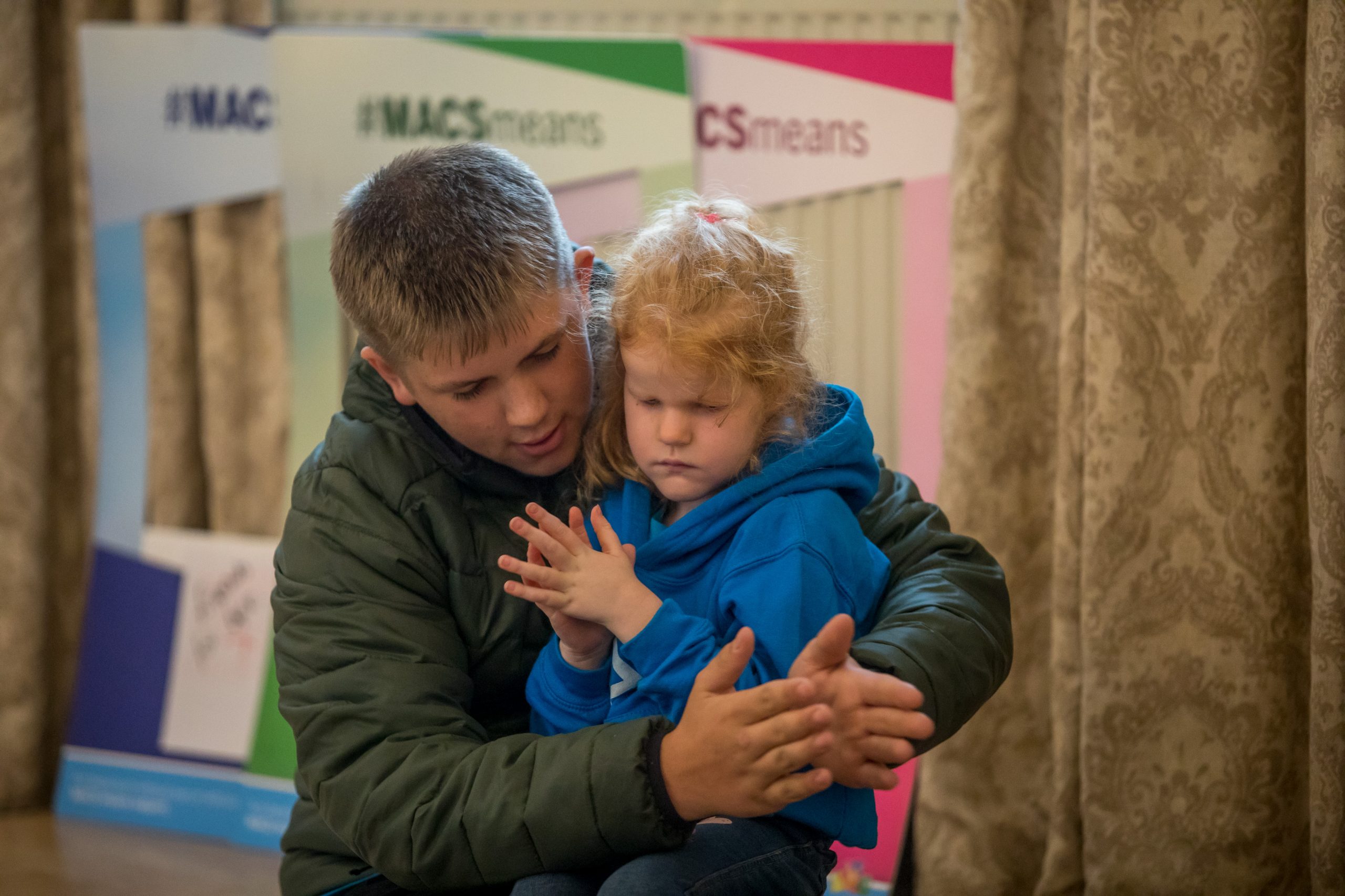 Image shows a MACS child clapping with an older sibling