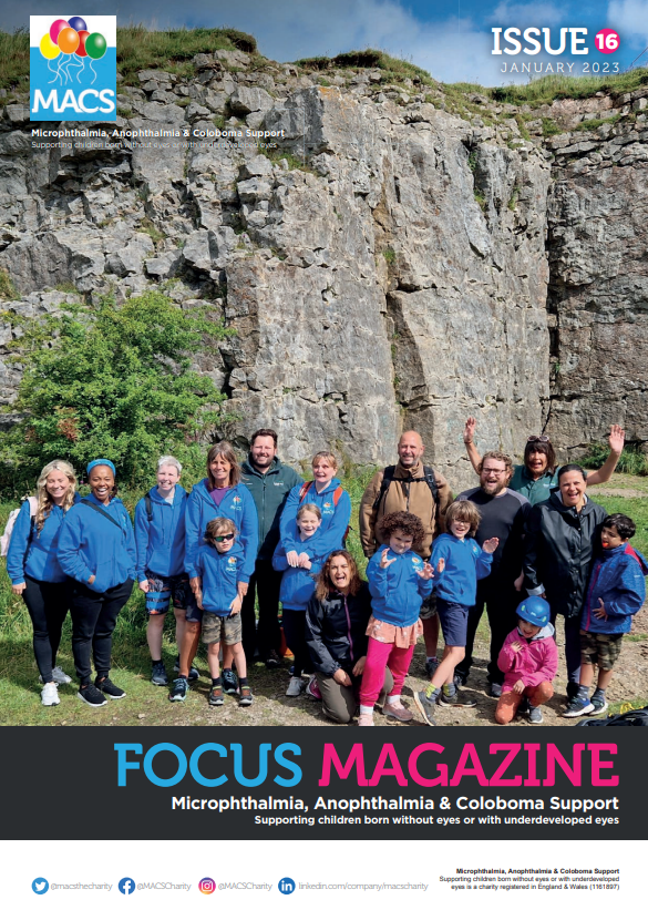 This cover shows a group of people gathered outdoors at the base of a tall, rugged rock formation. Many are wearing blue MACS T‑shirts, and some are bundled in jackets. The group is arranged across grass and pathways in a natural setting, with the cliff face rising behind them. The top section includes the MACS logo and “ISSUE 16.” The bottom banner features FOCUS MAGAZINE and the MACS support subtitle.