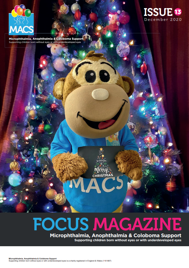 The cover shows a large friendly Macs the Monkey standing indoors in front of a decorated Christmas tree filled with multicoloured lights and ornaments. Macs the Monkey is wearing a blue MACS shirt and holding a rectangular sign with the MACS logo. The backdrop includes red curtains, giving a festive, staged atmosphere. The top includes the MACS logo and “ISSUE 13.” The bottom banner presents FOCUS MAGAZINE with the MACS support subtitle.