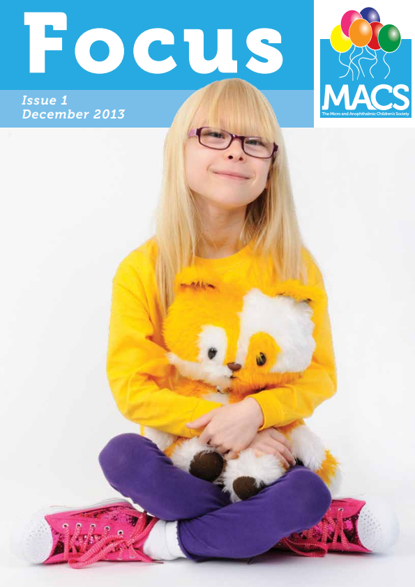 The cover shows a seated individual wearing a bright yellow sweatshirt featuring a large illustration of two owls. The person is sitting cross‑legged on a white floor, wearing purple trousers and pink shoes. A soft toy is resting on the person’s lap. The top section of the cover contains a light blue banner with the title “Focus”, the text “Issue 1 December 2013”, and the MACS logo with colourful balloons.