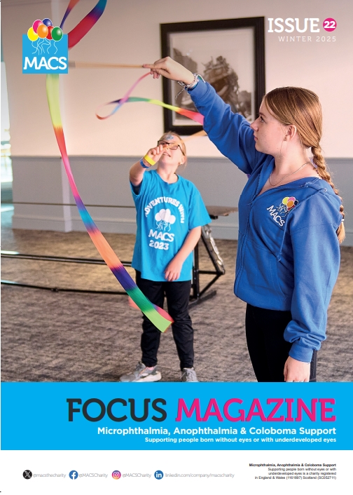 The cover features a person participating in an indoor activity involving a long, colourful ribbon streamer. The individual is mid‑movement, holding the ribbon high as it arcs gracefully across the space. Another person in the background is watching the activity. The setting appears to be a gym or hall with light‑coloured flooring and wall bars. The top banner includes the MACS logo and “ISSUE 22.” The bottom banner reads FOCUS MAGAZINE with the subtitle “Microphthalmia, Anophthalmia & Coloboma Support.”